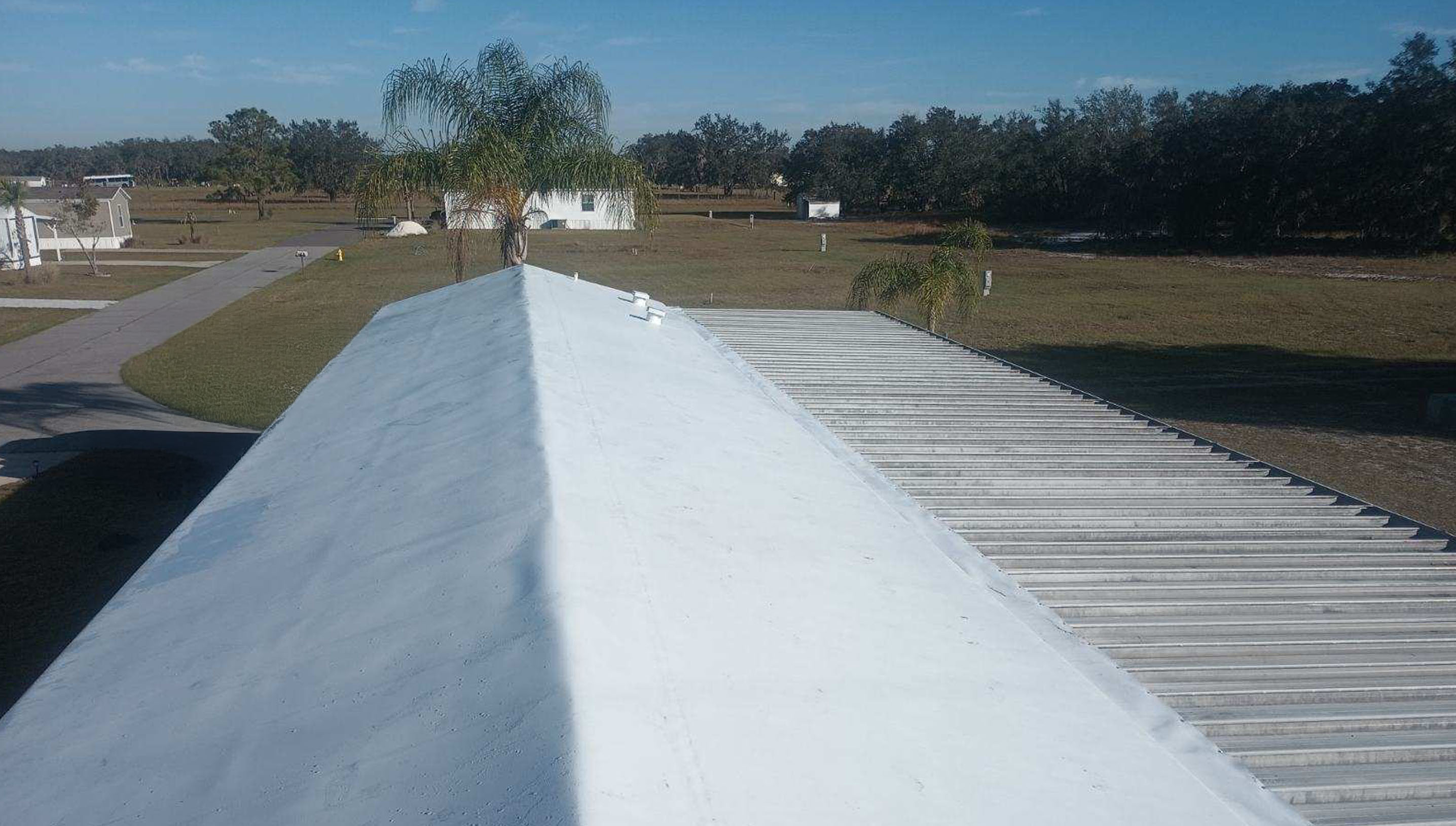 A white-coated rooftop with a corrugated roof section surrounded by grassy lawns.