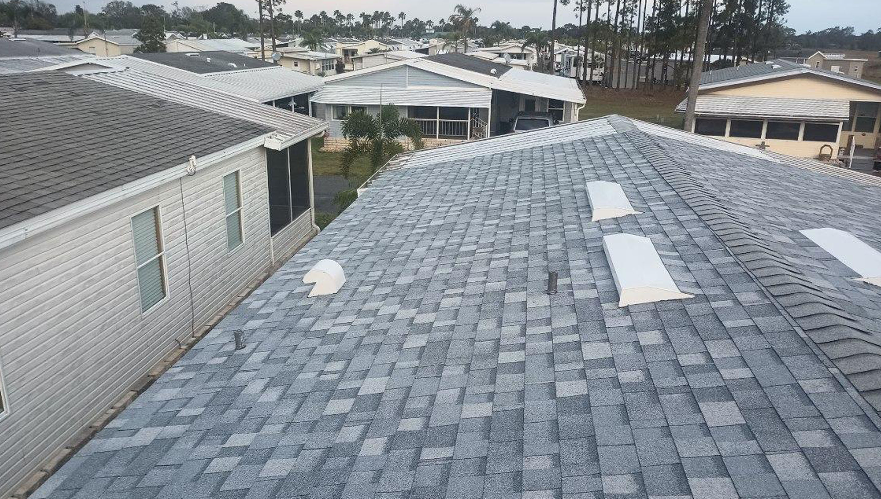 A rooftop with gray shingles and white vent fixtures in a residential neighborhood.