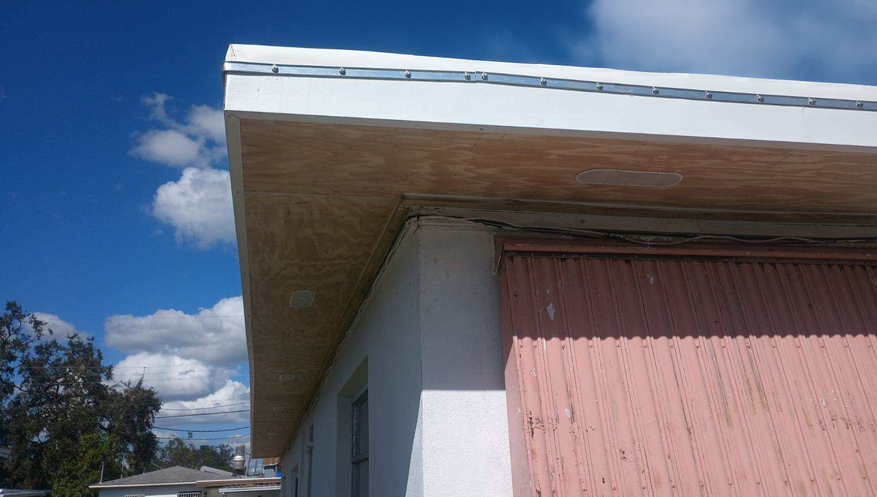 A building corner with a flat roof and white walls and pink walls.